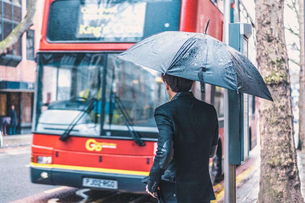 LONDON, UK - MARCH, 2016: Passenger under an umbrella is awaiting the red bus on a rainy day in London.