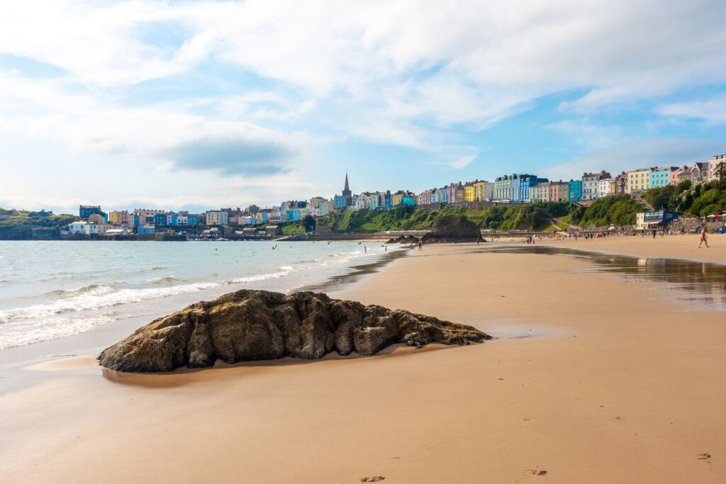 A view along The North Beach at Tenby in Pembrokeshire, Wales. Golden sand with beautiful coloured houses of Tenby Town Centre in the distance.