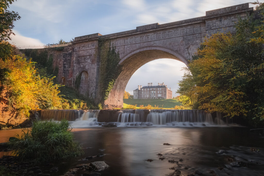 Dalkeith Country Park with waterfall and arch framing manor house on a sunny autumn afternoon makes for an ideal day trip from Edinburgh in Scotland.