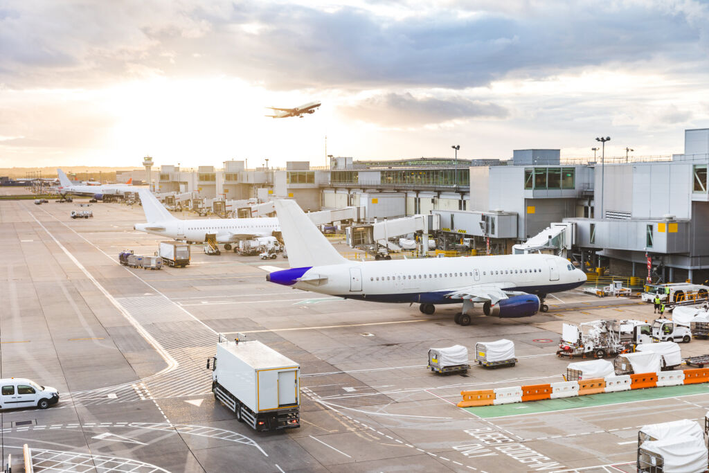 Tętniący widok na lotnisko z samolotów i pojazdów serwisowych o zachodzie słońca. Lotnisko w Londynie z samolotami przy bramach i starcie, ciężarówki dookoła i słońce zachodzi w tle. Koncepcje podróży i przemysłu