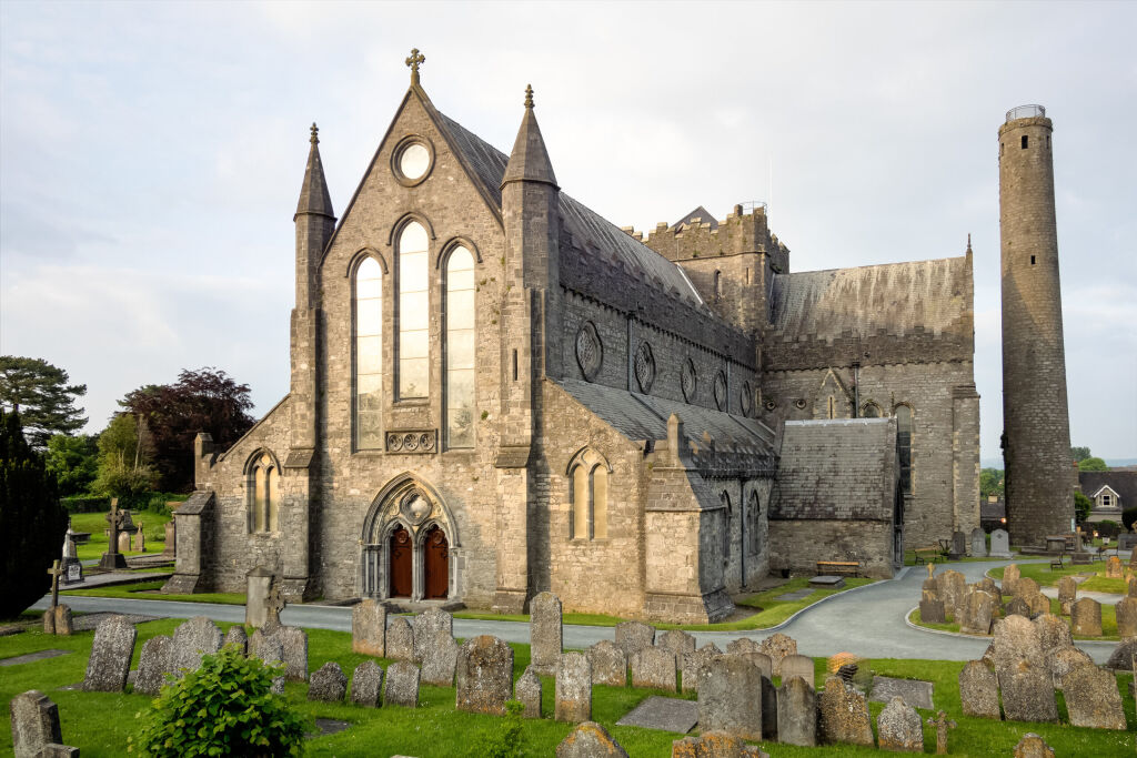 View of st Canice's cathedral, a mediaval religious monument of Kilkenny in Ireland made of grey stones. There is a cimetetry with tombs near the building.