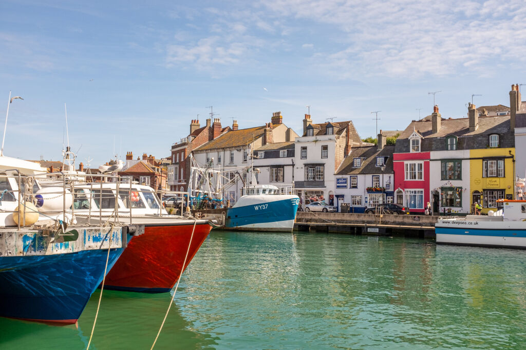 Weymouth, England - June 29, 2015: Boats moored at Weymouth harbour, with shops and houses in the background, on a sunny summer day in Dorset, England