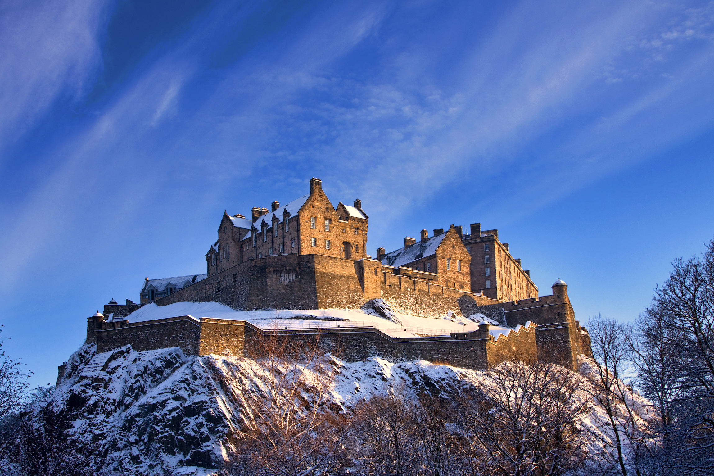 Zamek w Edynburgu odkurzony śniegiem świeci w późnym popołudniem zimowego zachodu słońca.