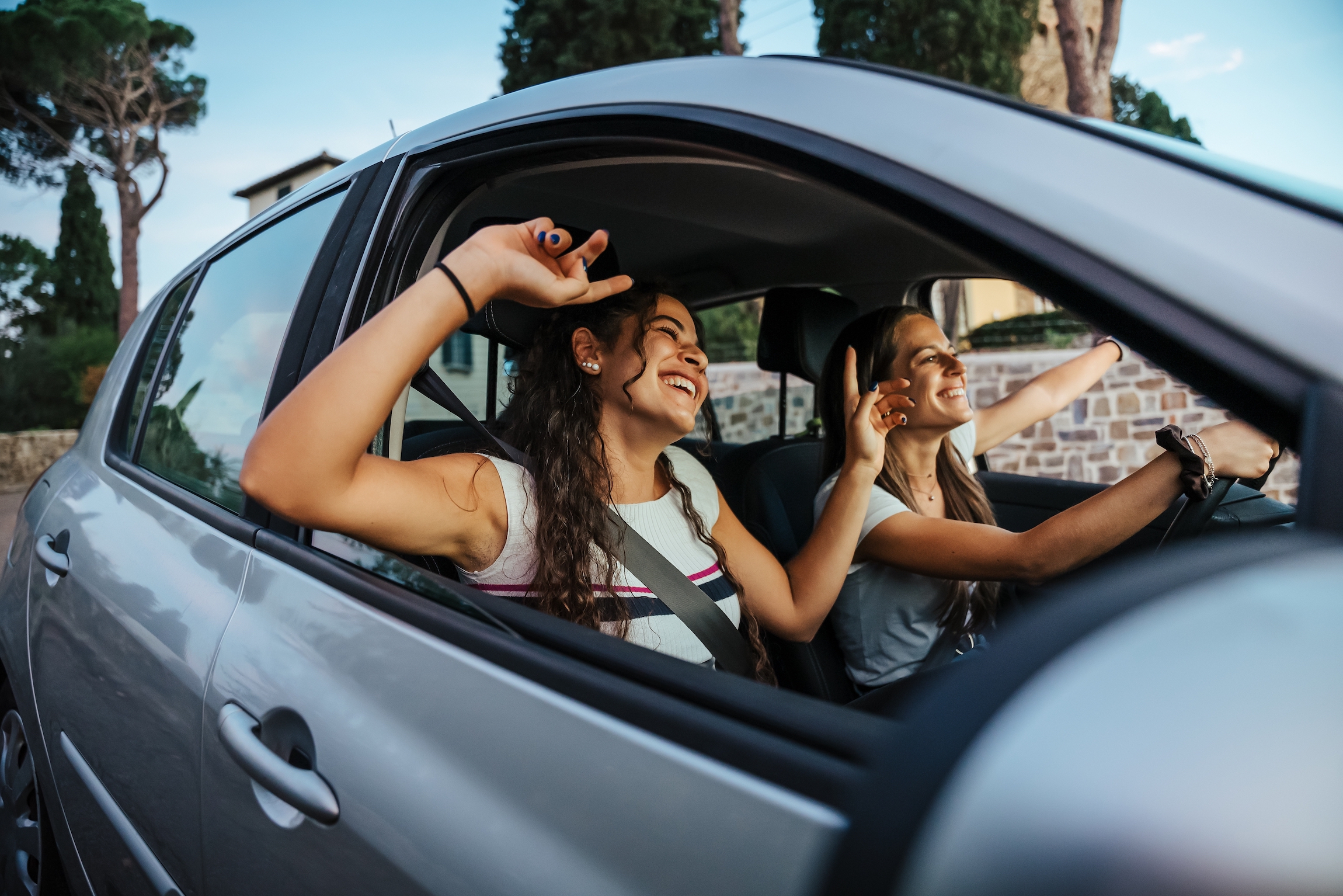 Dwie młode kobiety śpiewają piosenkę w radiu i tańczą w samochodzie podczas letniej wycieczki - Najlepsi przyjaciele bawiący się razem podczas jazdy po okolicy - Uśmiechnięci milenialsi w chwili relaksu