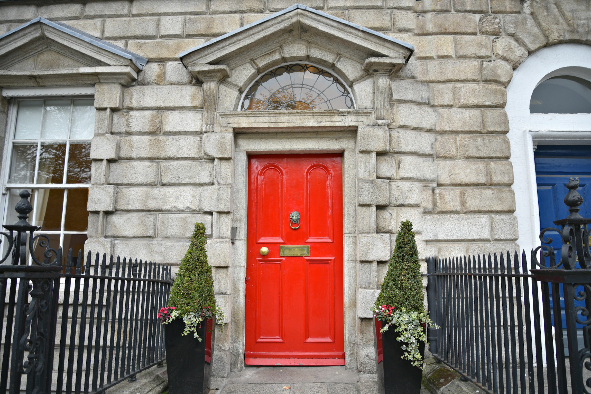 Kamienna fasada budynku w stylu georgiańskim z jasnoczerwonymi drzwiami wejściowymi i mosiężną klamką na Merrion Square w Dublinie, Irlandia. 