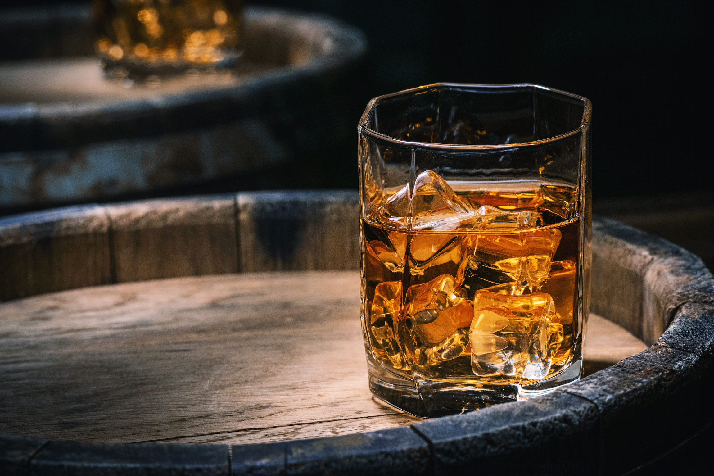 Butelka i szklanka whisky z lodem na drewnianym tle. Szklanka szkockiej whisky z lodem stoi na rustykalnej beczce whisky. Whisky z lodem.